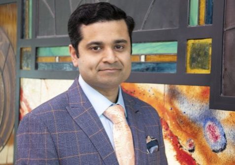 Krishna headshot Krishna wearing blue checked suit with pink tie, smiling got the camera
