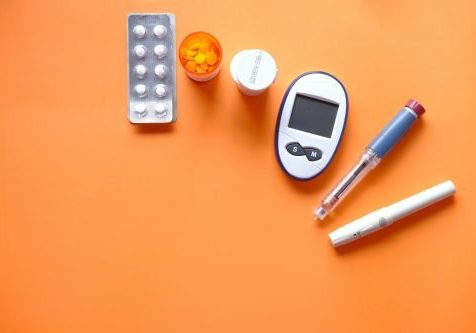 diabetes insulin pen, diabetic measurement tools and pills on orange background